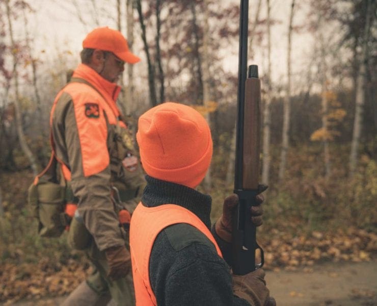 An adult hunter mentors a kid on a grouse hunt.