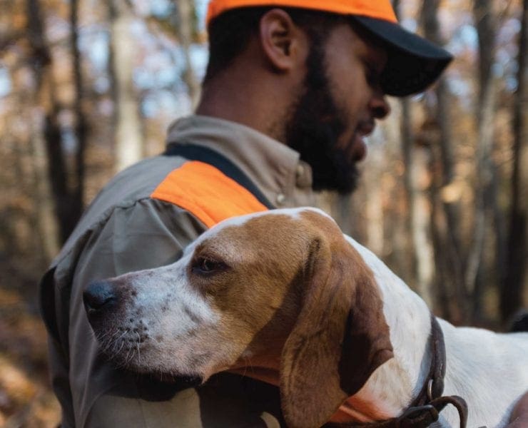 An African-American upland hunter in a field with his bird dog.