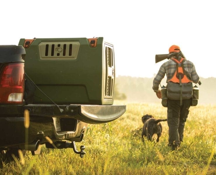 A primos kennel sitting on a tailgate with a bird dog and upland hunter.
