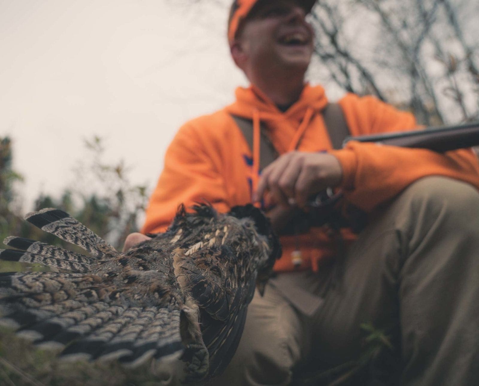 an upland hunter holds a ruffed grouse with friends.