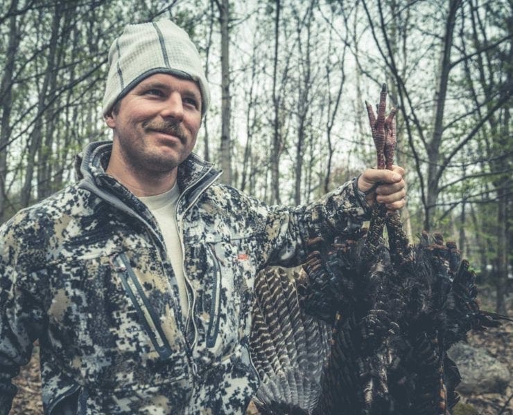 A new turkey hunter holds up their first turkey up with joy.