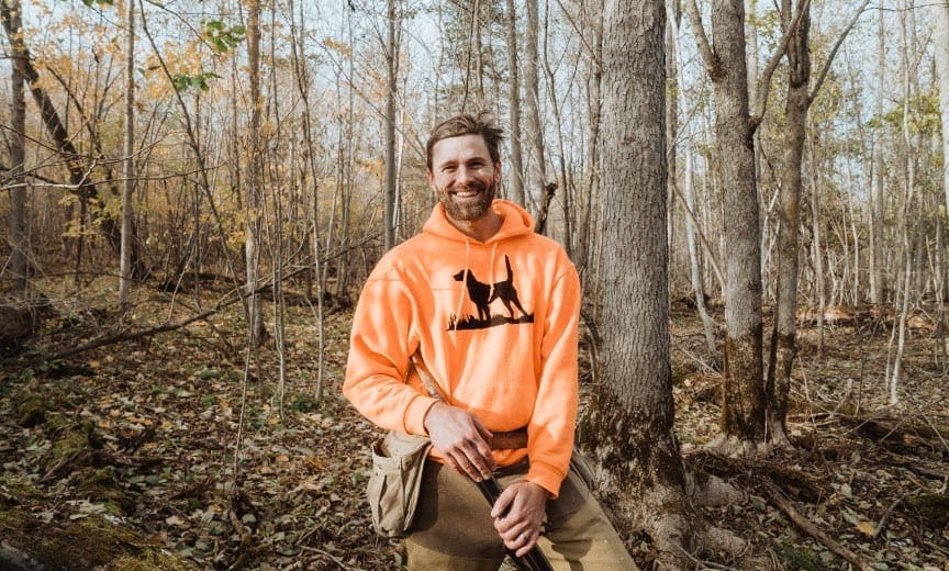 A ruffed grouse hunter standing in a cover with a side by side shotgun. 