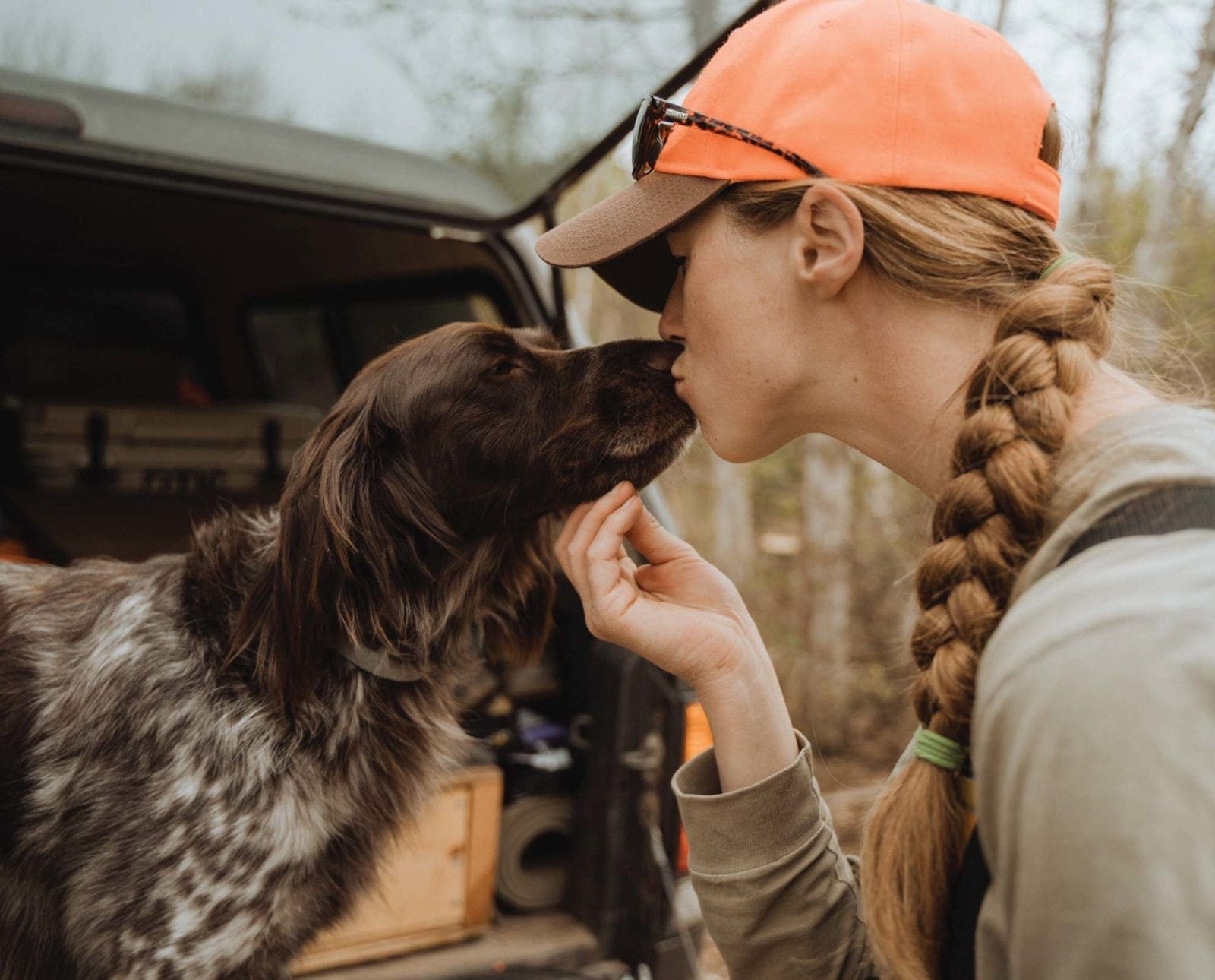 A woman kisses her pointing dog.