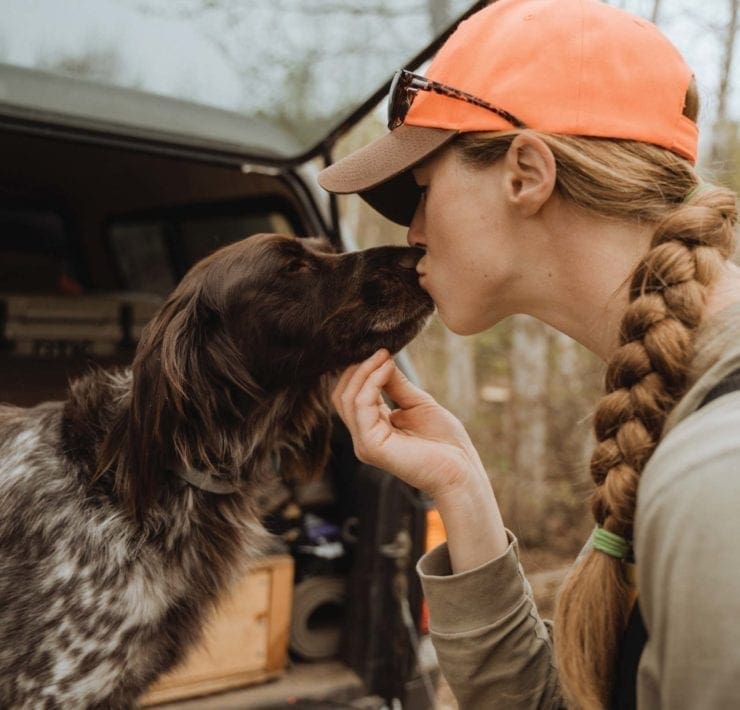 A woman kisses her pointing dog.