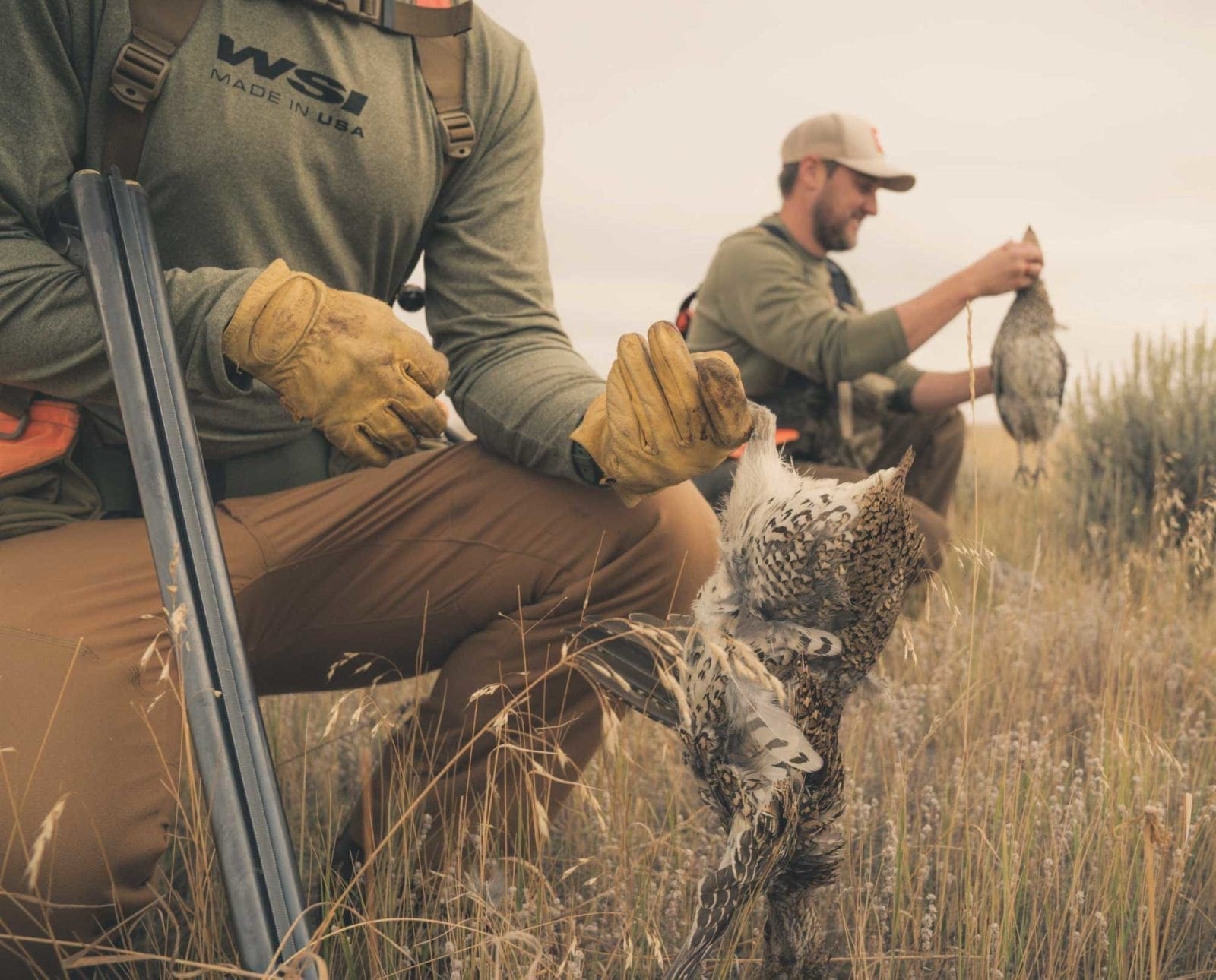 A bird hunter holds sharp-tailed grouse with his shotgun in hand.