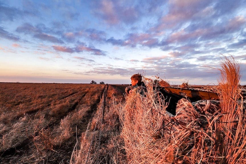 A young boy stands in a duck hunting blind in a field
