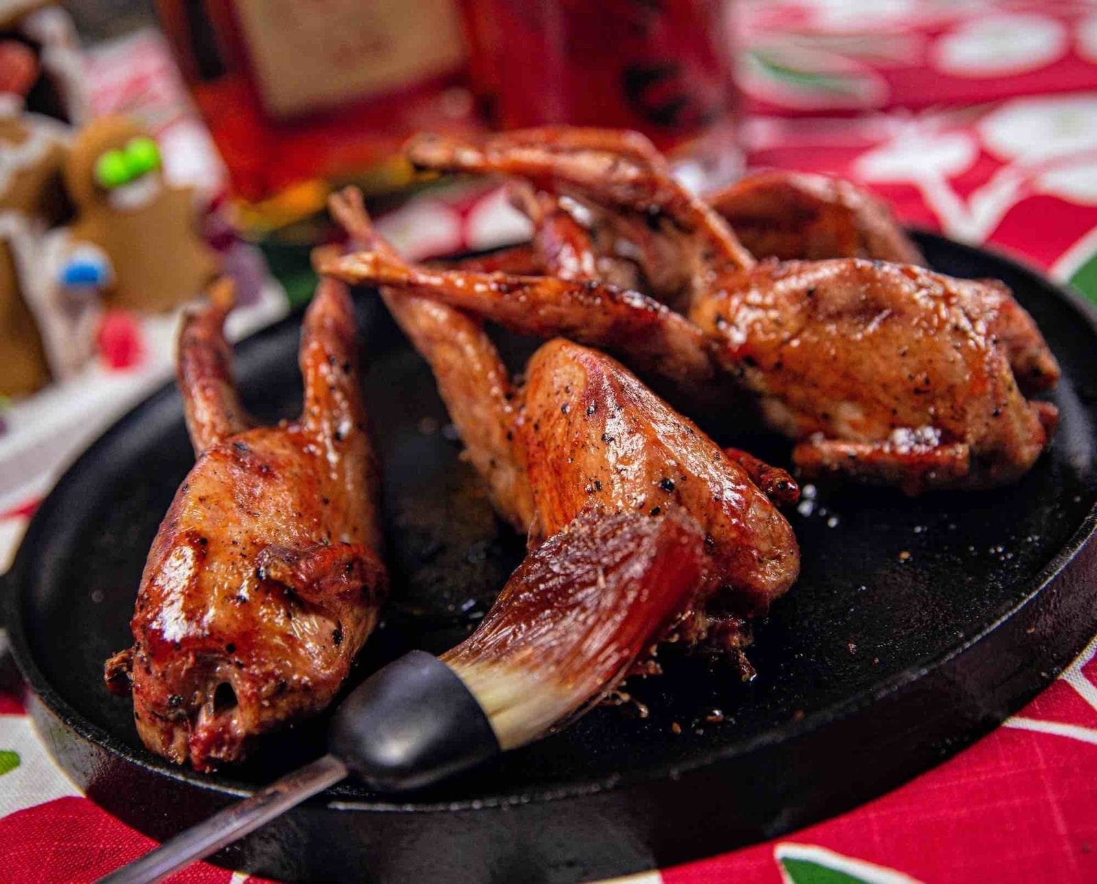 Four cranberry glazed quail on a cast iron skillet with a basting brush