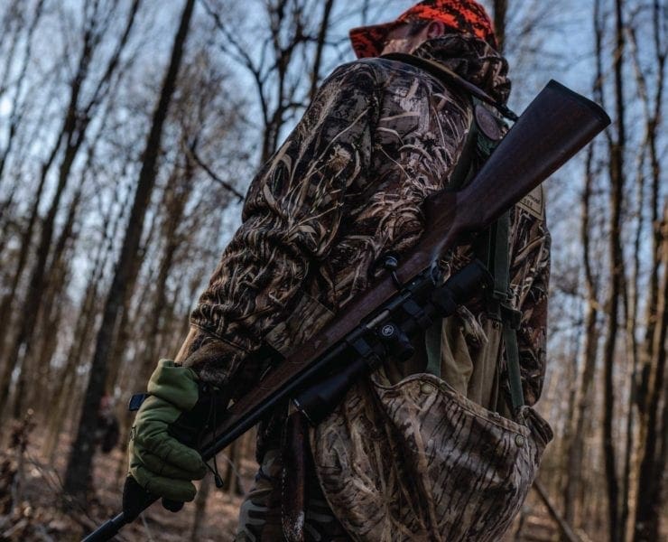 A squirrel hunter stands in the woods with a gun