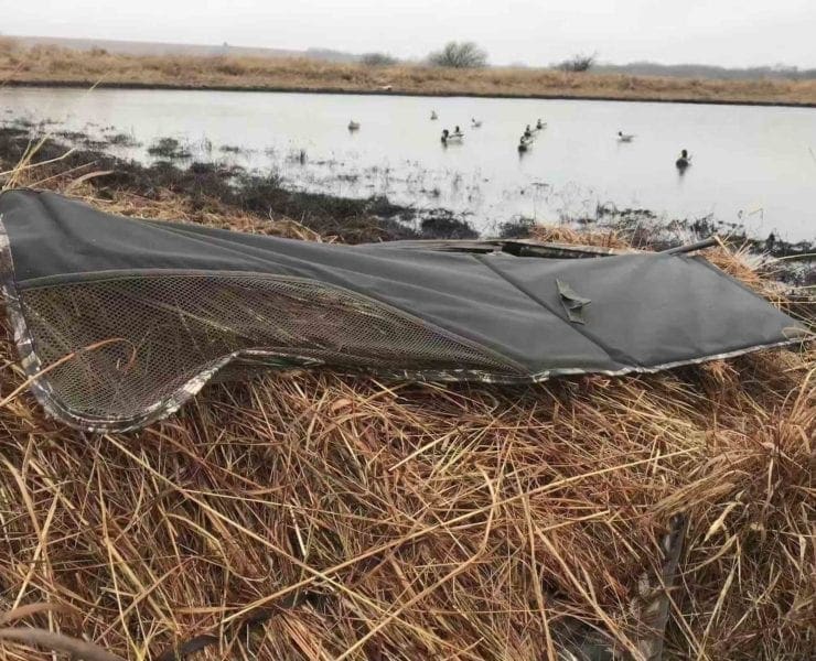 A layout blind for duck hunting next to decoys on a pond