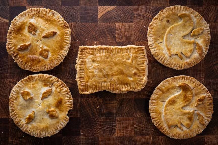 Five individual, savory, meat pies on a wood surface