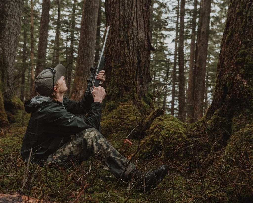 A sooty grouse hunter sets up for a shot with a rifle