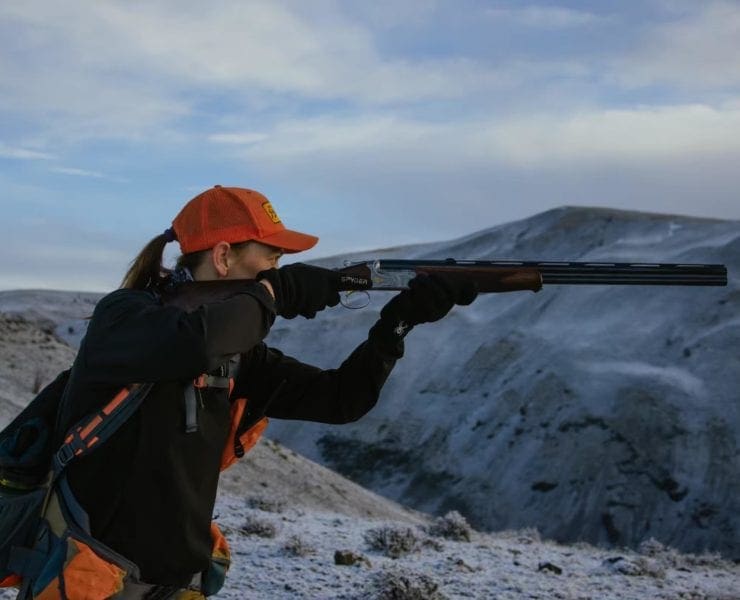A woman points an over/under shotgun while bird hunting