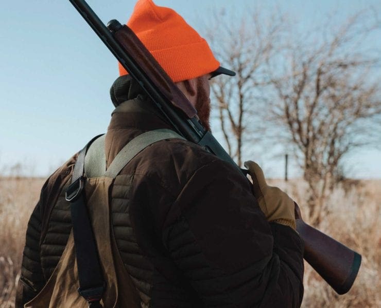 A hunter carrying a Remington 870 pump shotgun in the field.