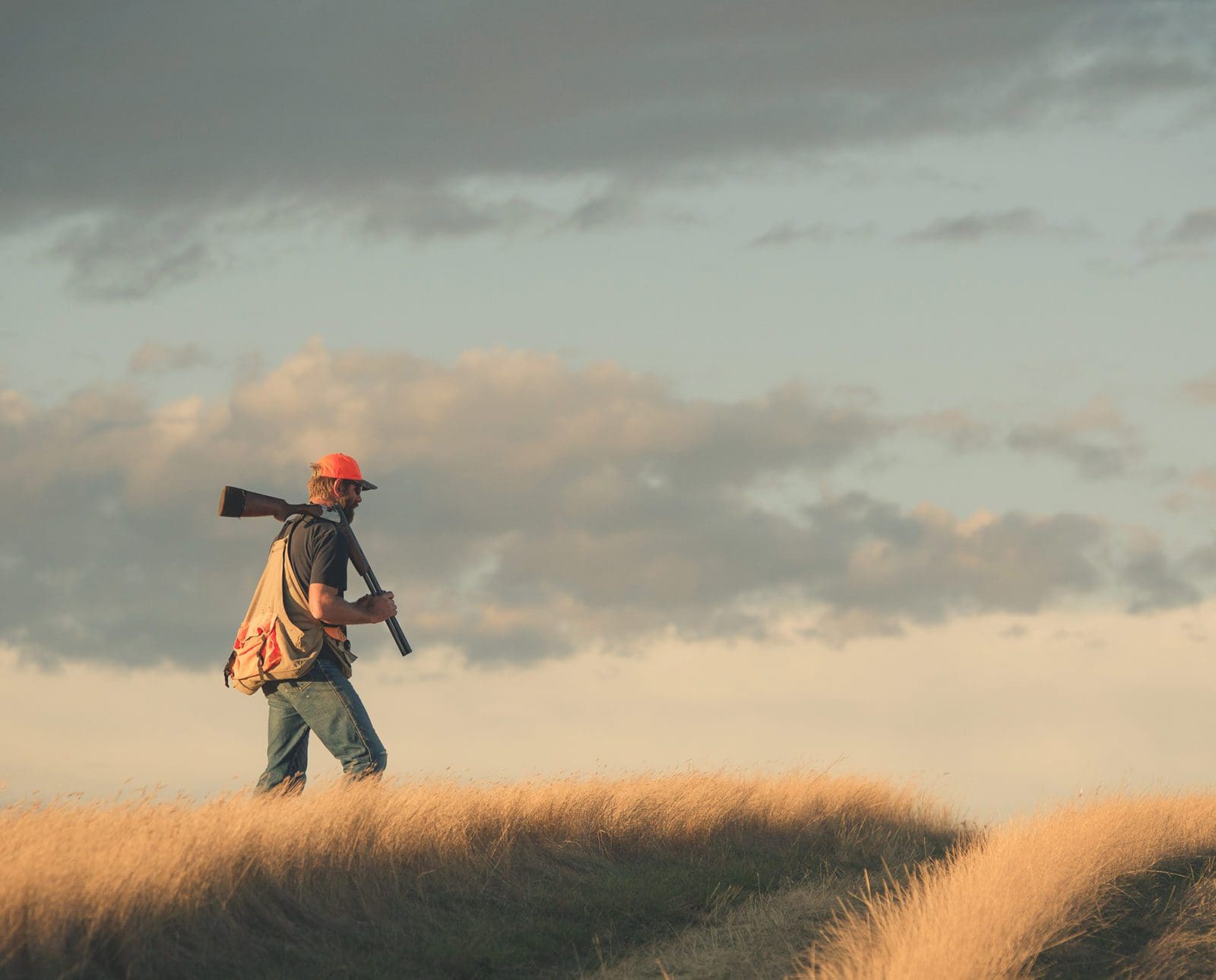 A hunter walks over a hill in a grassland area.