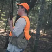 A young hunter holds a youth shotgun wearing blaze orange in the woods
