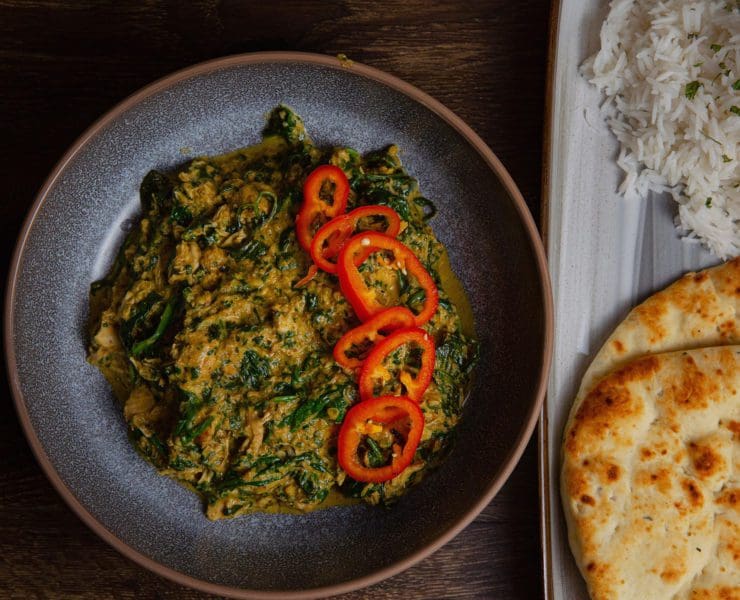 Palak Pheasant rests in a bowl next to a side of naan bread.
