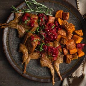 Roasted quail is garnished with cranberry sauce.