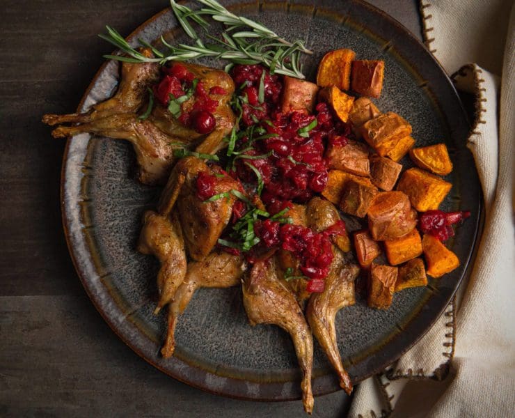 Roasted quail is garnished with cranberry sauce.