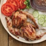 Lemongrass Grilled Quail plated with rice, tomatoes, lettuce, and cucumber in traditional Vietnamese style