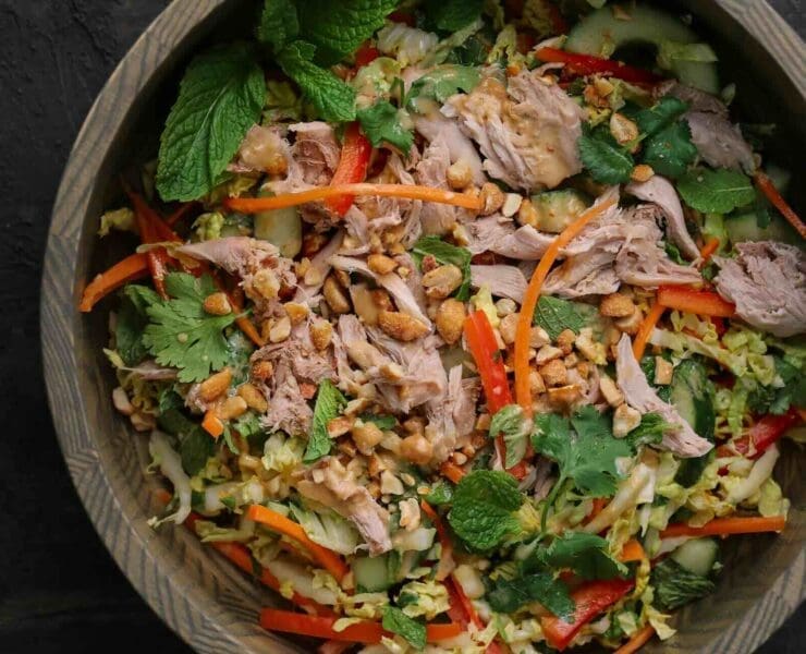 Cooked chukar meat on a bed of cabbage, carrots, cucumbers, and other salad vegetables served in a wooden bowl