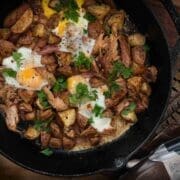 Corned pheasant hash with fried egg and red potatoes in a cast iron skillet with an accent of pheasant feathers