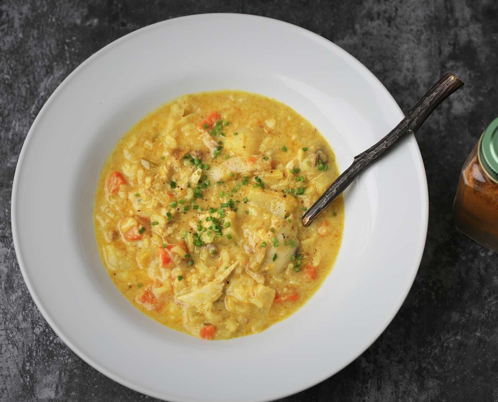 A bowl of quail mulligatawny soup in a white bowl on a dark slate background