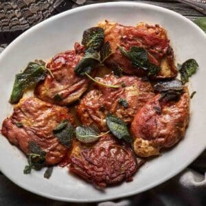 A white platter of prepared ruffed grouse saltimbocca with sage leaves