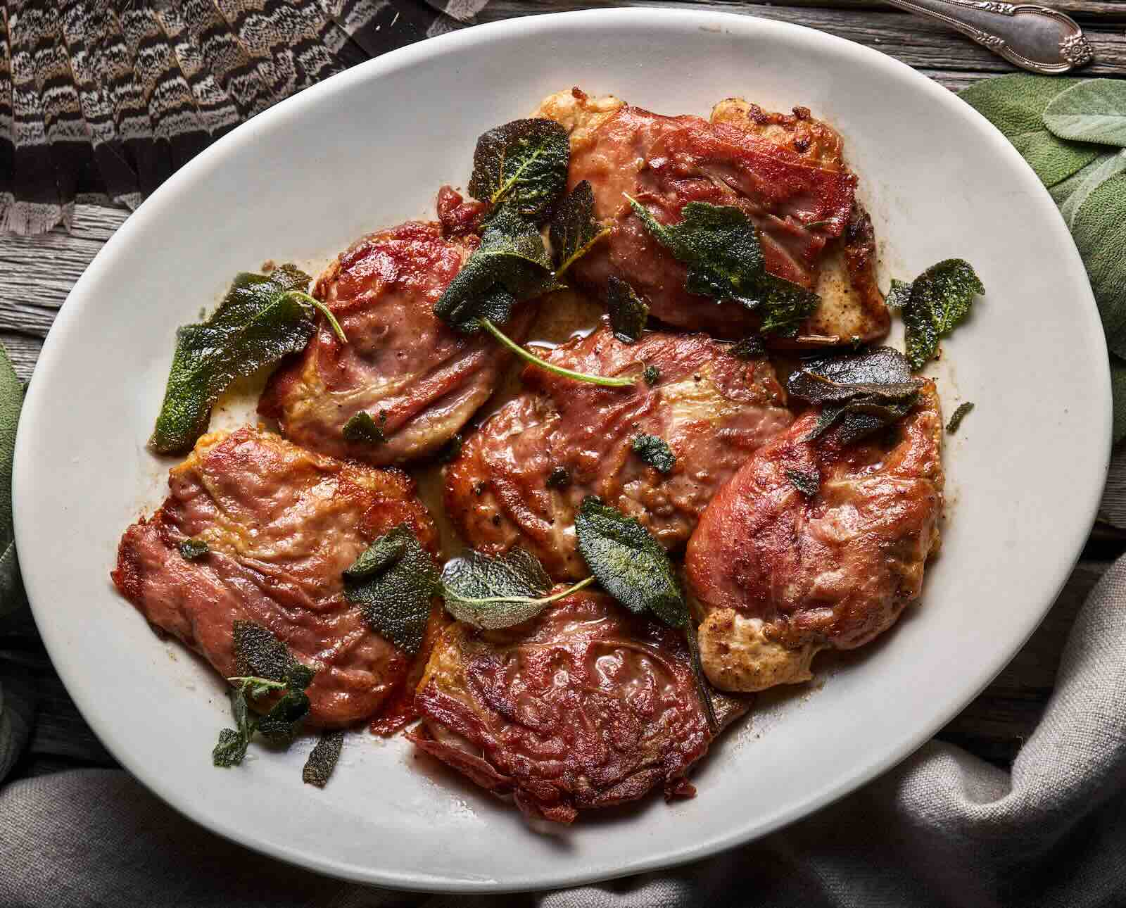 A white platter of prepared ruffed grouse saltimbocca with sage leaves