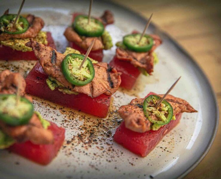 An appetizer dish of watermelon, pheasant, and jalapeno on toothpicks served on a platter
