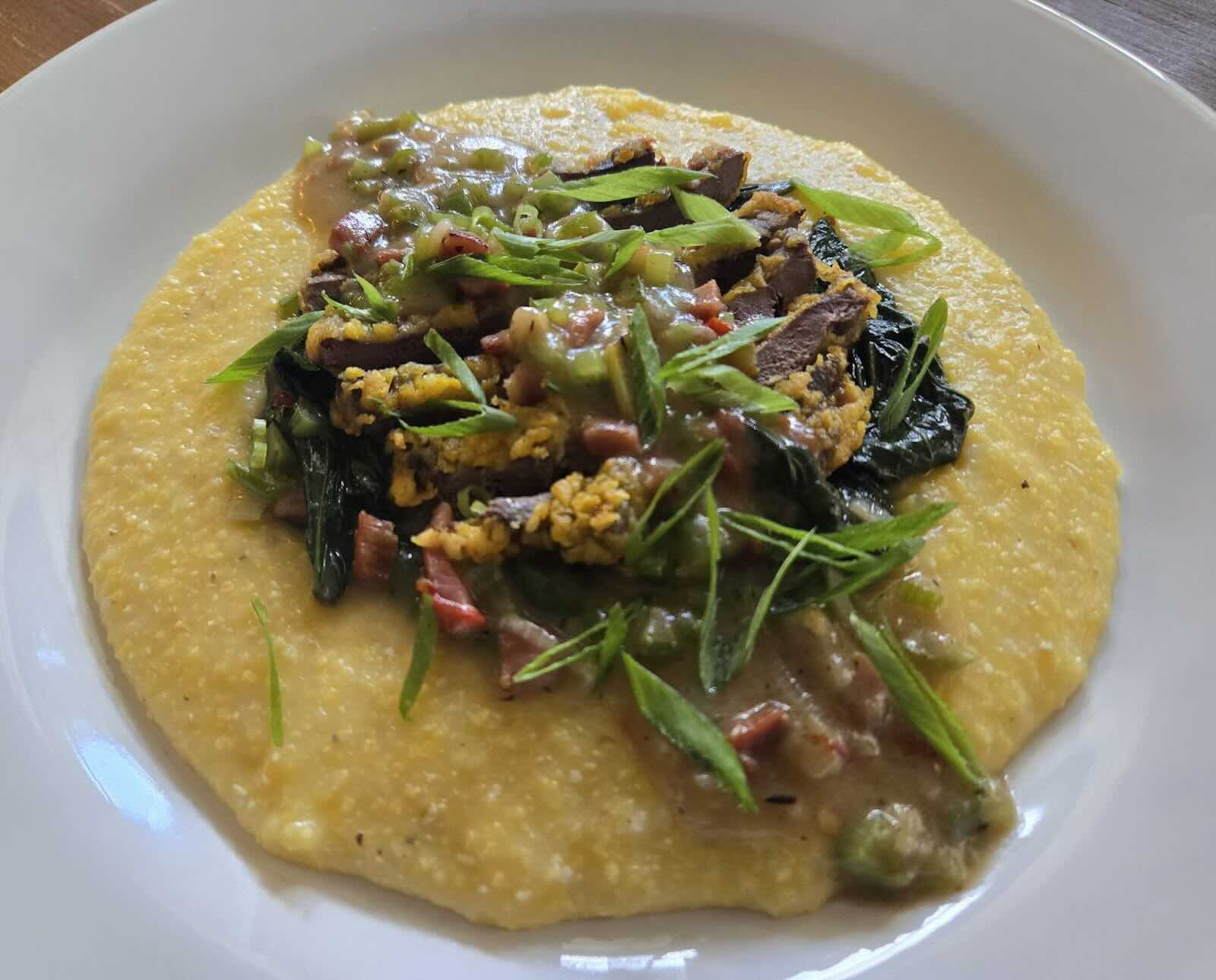 A serving of fried woodcock and yellow grits topped with fresh scallions on a white plate