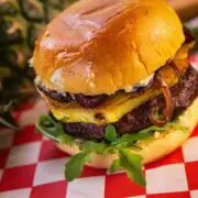 A burger made with ground goose meat topped with pineapple and lettuce on a checkered paper