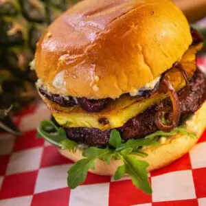 A burger made with ground goose meat topped with pineapple and lettuce on a checkered paper