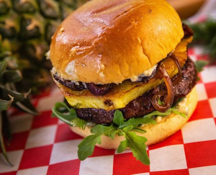 A burger made with ground goose meat topped with pineapple and lettuce on a checkered paper