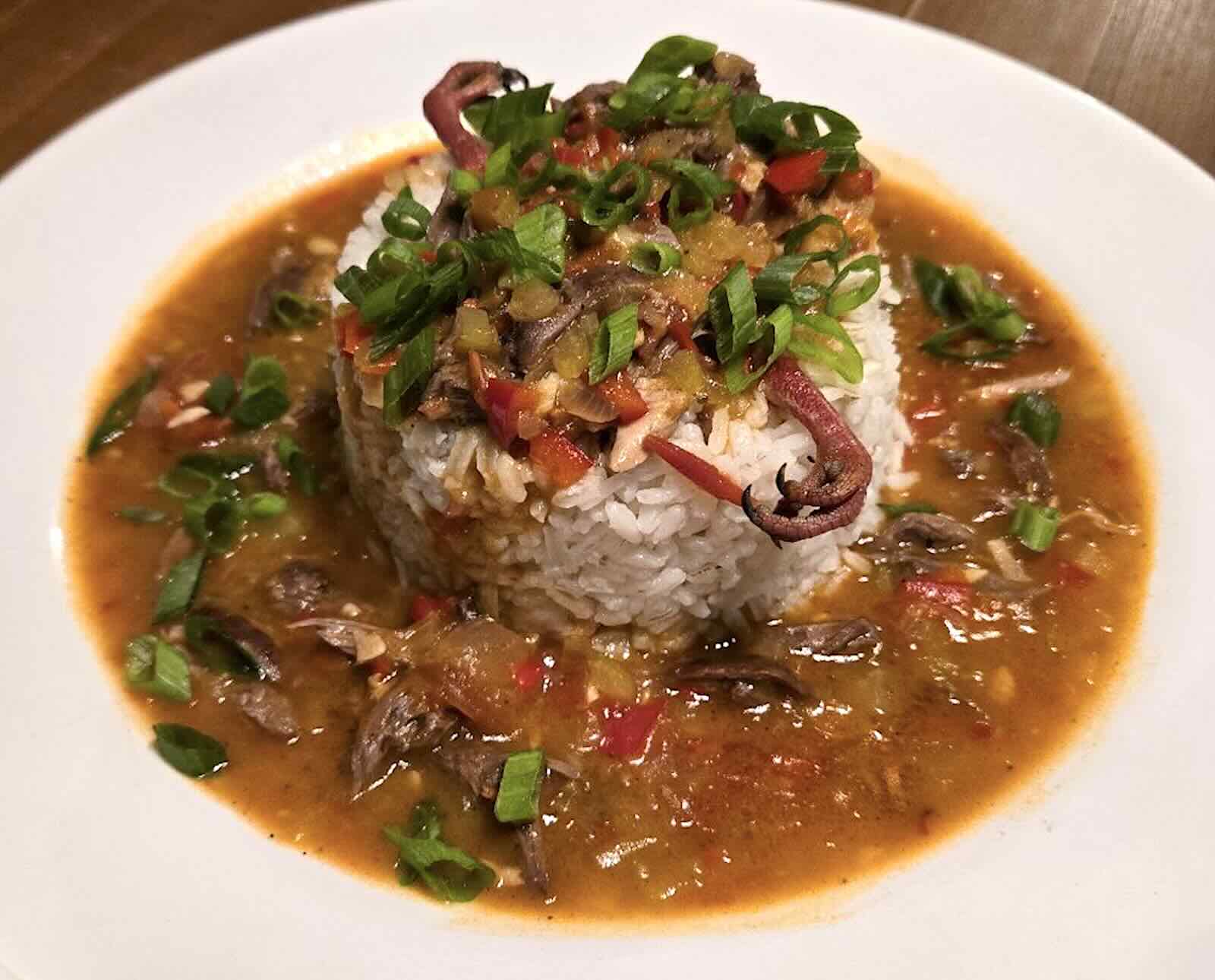 A serving of white rice covered in a sauce and dove meat, served on a white plate