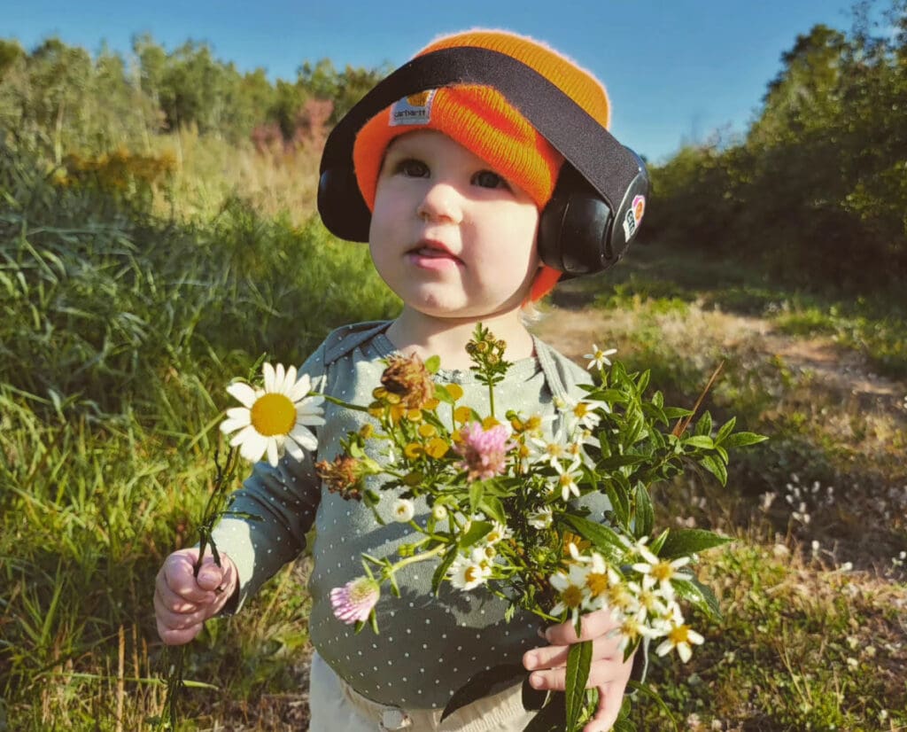 A toddler picks flowers while out hunting. 