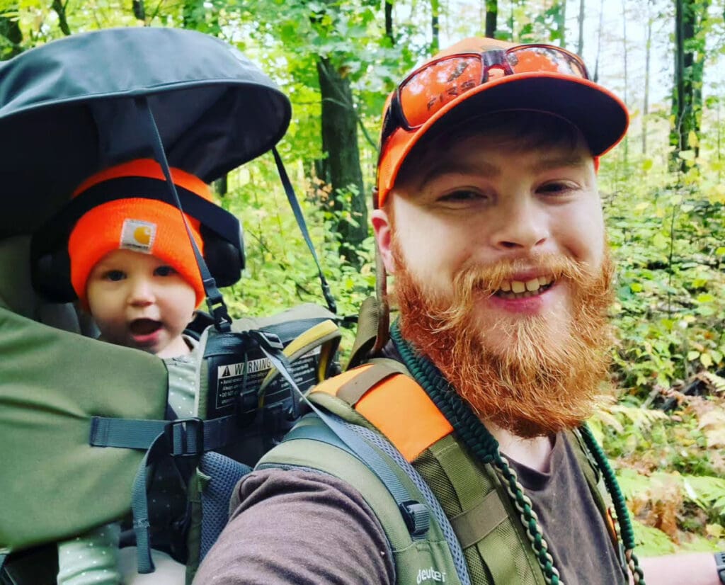 A father carries a toddler on his back while hunting. 