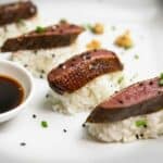 Thin slices of sous vide duck breast served atop sushi rice and with soy sauce for dipping