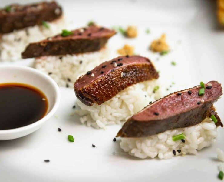 Thin slices of sous vide duck breast served atop sushi rice and with soy sauce for dipping