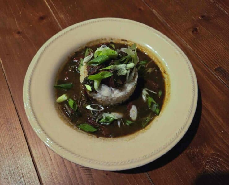 A white dish filled with rice and gumbo on a wood plank background