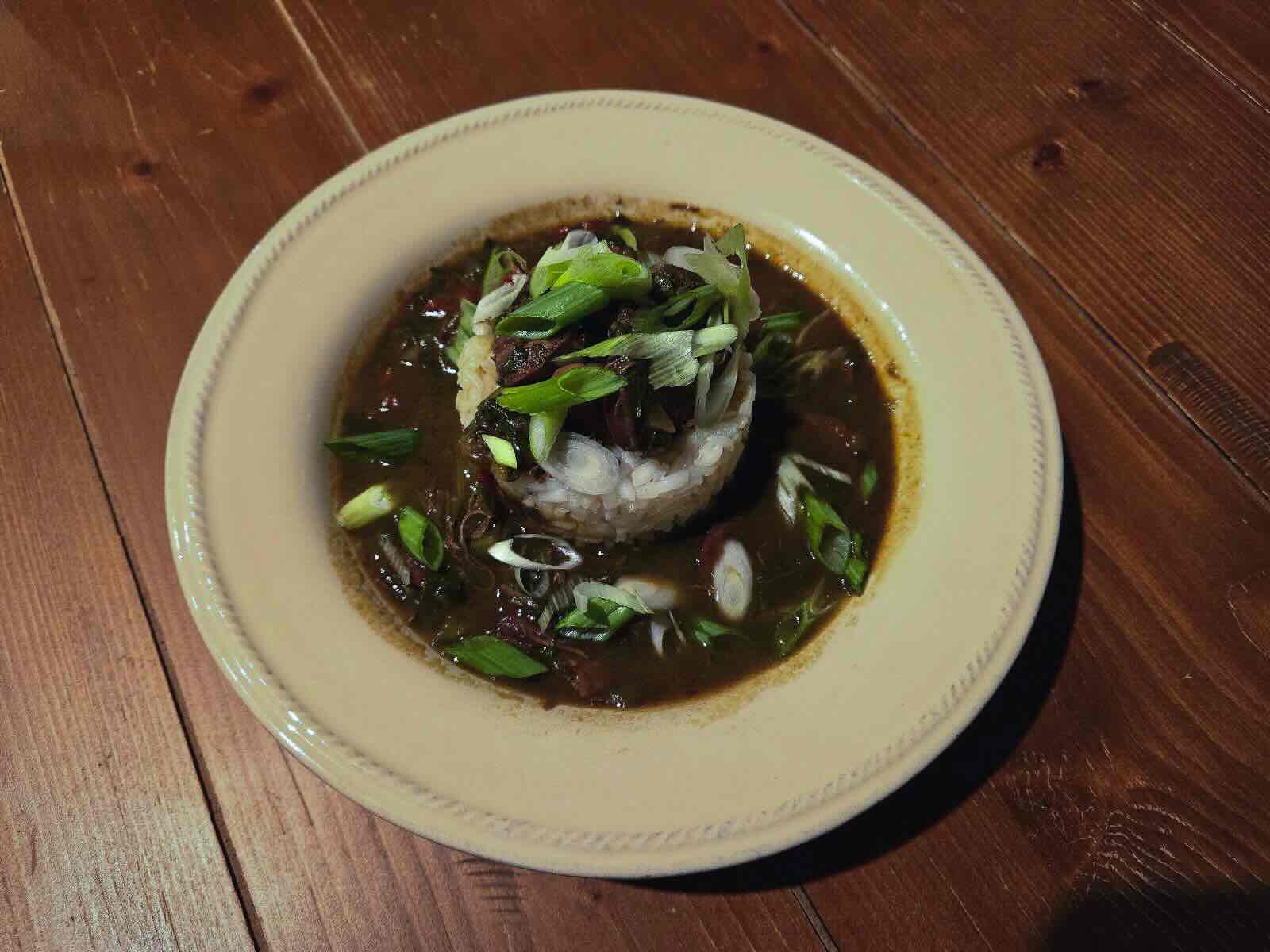 A white dish filled with rice and gumbo on a wood plank background