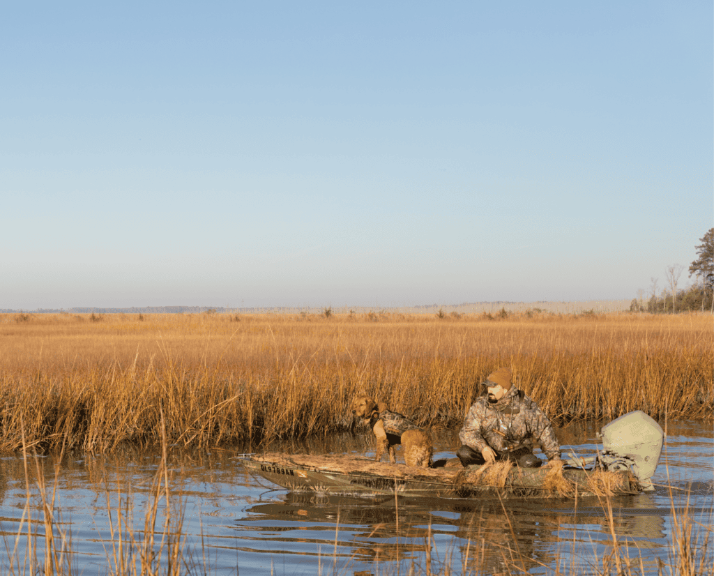 A waterfowl hunter and his golden retriever float in a boat in black duck habitat.