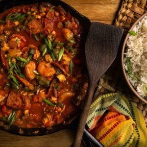 Upland bird jambalaya served in a cast iron skillet with a bowl of white rice and garnishes