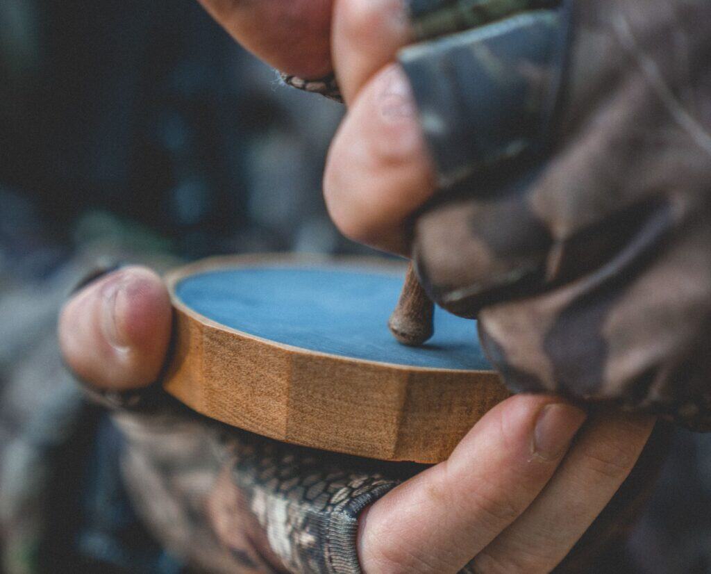 A turkey hunter wearing camo gloves and using a slate or pot call.