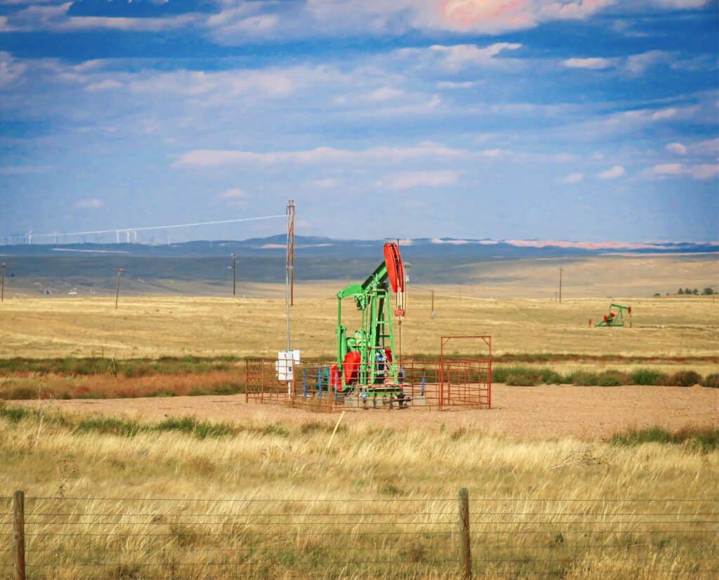 An oiljack operates in a grassland near some small mountains.