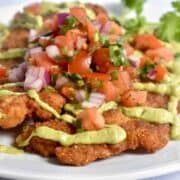 Mexican-inspired wild turkey schnitzel with avocado crema and pico de gallo served atop the breaded schnitzel, all atop a white plate