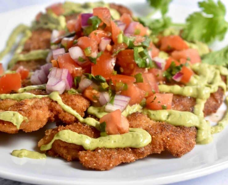 Mexican-inspired wild turkey schnitzel with avocado crema and pico de gallo served atop the breaded schnitzel, all atop a white plate