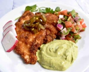 Mexican-inspired wild turkey schnitzel with avocado crema and pico de gallo served on the side, all atop a white plate