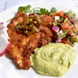 Mexican-inspired wild turkey schnitzel with avocado crema and pico de gallo served on the side, all atop a white plate