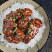 A serving of fried turkey breast in a Chinese orange sauce, topped with green onions and sesame seeds, served atop white rice on a plate