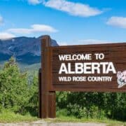A sign that says "welcome to Alberta" along a road winding through mountains in Canada.